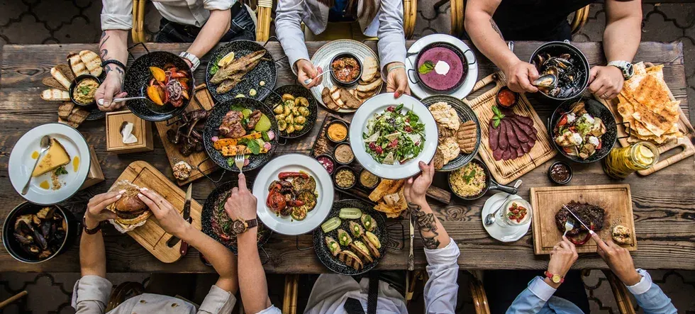 A long table seen from above, covered in shared plates with hands reaching across it