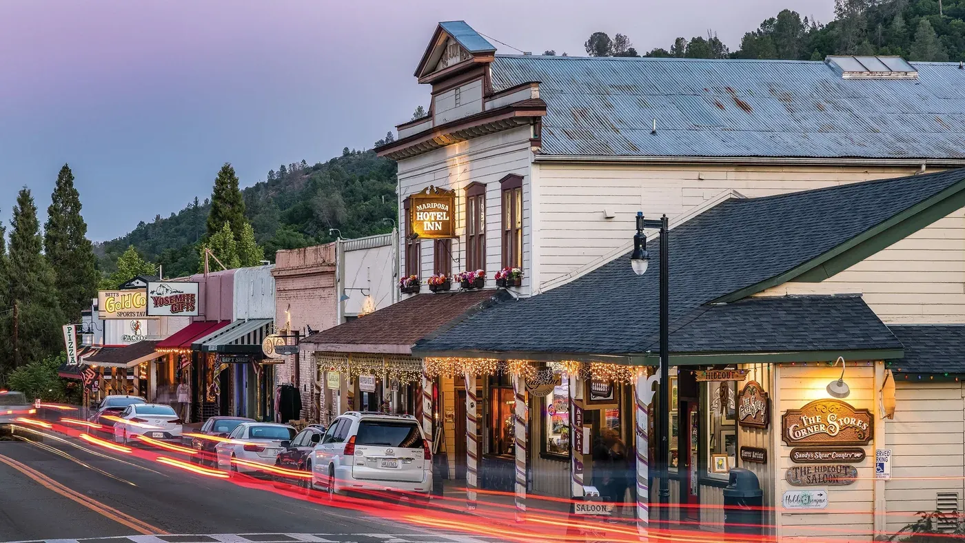 Mariposa’s main street at dusk, lit shopfronts and the old hotel above passing traffic